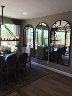 a dining room table and chairs with large mirrors on the wall behind them in front of windows