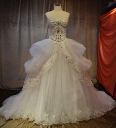 a white wedding dress on display in front of a red curtain