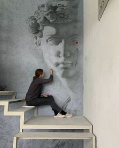 a woman sitting on top of a set of stairs next to a wall with a painting