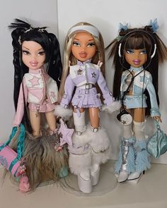 three dolls standing next to each other in front of a white wall and two are holding purses