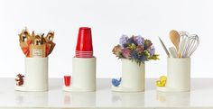 three white vases with flowers and kitchen utensils in them on a table