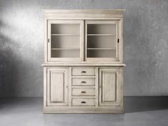 an old white china cabinet with glass doors on the top and bottom, in front of a concrete wall