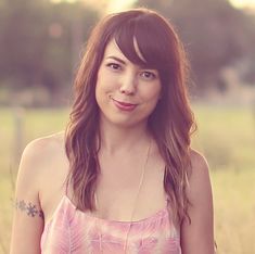 a woman standing in a field with her hand on her hip and looking at the camera