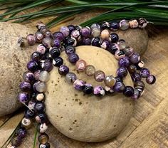 a purple beaded necklace sitting on top of a rock next to a green plant