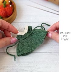 two hands are holding a green crocheted bag on a white table with fruit in the background