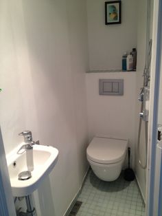 a white toilet sitting in a bathroom next to a sink and shower head mounted on the wall