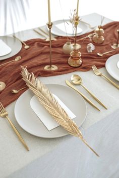 the table is set with white plates and gold cutlery, silverware, and napkins