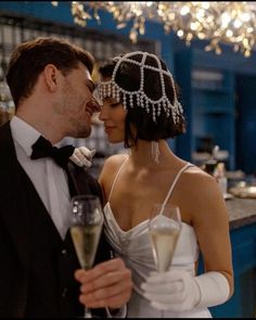 a bride and groom holding champagne flutes in front of a chandelier filled with lights