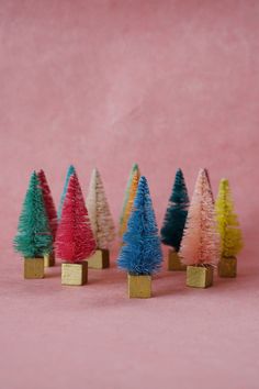 small colorful trees are lined up in gold holders on a pink surface, with one standing out from the others