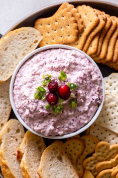 a bowl filled with dip surrounded by crackers and cranberries