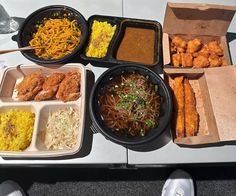 there are many different foods in the trays on the table, including rice noodles and fried chicken