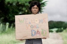 a young boy holding a sign that says welcome home to his dad on the road