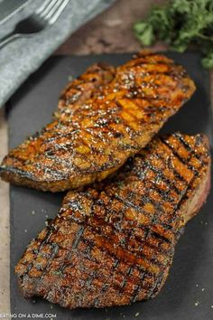 two steaks on a black cutting board next to some parsley and a fork