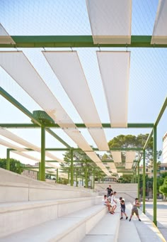 several people are sitting on the steps under an awning in a public area with concrete stairs and green railings