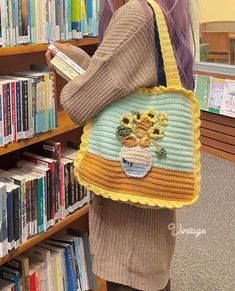 a woman holding a crocheted bag in front of a book shelf filled with books