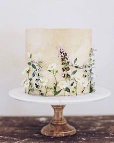 a white cake with flowers on it sitting on top of a wooden table next to a wall