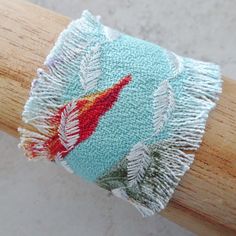 "Lovely tropical beach themed bracelet features an aqua blue tropical bark cloth fabric with a frayed edging and a decorative embroidered leaf pattern ivory thread top stitching.  This bracelet is comfortable to wear and the crimp portions of fabric are linked with a brass metal flower toggle closure. The width of the fabric portion of the bracelet is 2\" and the length of the bracelet is 6 1/2 \". All of my jewelry items come boxed and lace ribbon tied and tagged for easy gifting." Bohemian Light Blue Friendship Bracelets For Beach, Handwoven Blue Bracelets For The Beach, Blue Handwoven Bracelets For Beach, Beach Themed Bracelet, Fabric Cuff Bracelet, Blue Floral Fabric, Bark Cloth, Beautiful Chokers, Embroidered Leaves