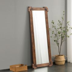 a wooden mirror sitting on top of a floor next to a potted plant and basket