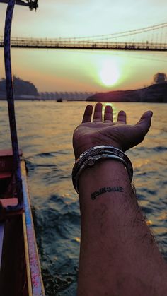 a person's hand on the edge of a boat in front of a bridge