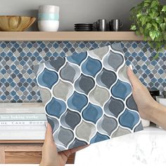 a person holding up a blue and gray tile pattern on a counter top next to books