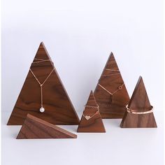 three wooden christmas trees with necklaces on them and one has a white pearl in the middle