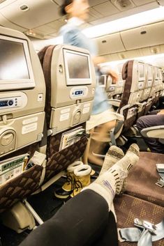 the inside of an airplane with people sitting on seats and looking at televisions in the back