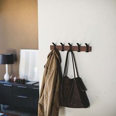 a coat rack with two coats hanging from it's hooks and a purse on the wall