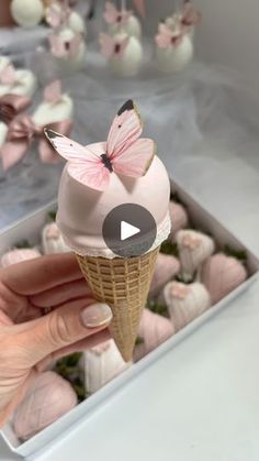 a hand holding an ice cream cone with pink butterflies on top and white balls in the background