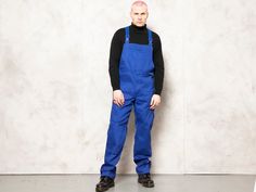 "Full and ready vintage 90's men work dungarees in indigo blue. Classic flap closure and durable fabric to accompany you on all kinds of works. Multiple front pockets. CONDITION: good vintage; has a spots here and there, see the last picture. MODEL is 6.4 ft (196 cm) tall, size XL - and he wears the size available. SIZE: Suggested size: L. To be sure the size will fit check the sizing details listed below. FLAT Measurements Side to side (waist): 16 1/2 \" / 42 cm Length: 51 \" / 129,5 cm Inseam: Blue Utility Bib Front Overalls, Blue Utility Overalls With Bib Front, Garage Fashion, Vintage Suede Coat, Men Jumpsuit, 90s Men, Mens Overalls, Mens Sherpa, Jumpsuit Blue