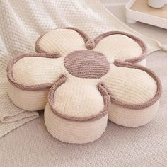 four knitted flower cushions on a bed with a white blanket and tray in the background