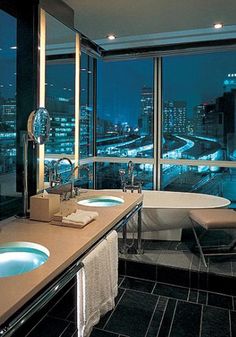 a bathroom with two sinks and a tub in front of a large window overlooking the city