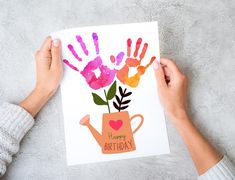 two hands holding up a card with the words happy birthday written on it and flowers in a watering can