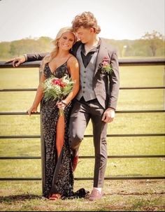 a young man and woman dressed in formal wear standing next to each other near a fence