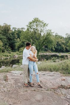 a man and woman hugging each other in front of a river surrounded by green trees