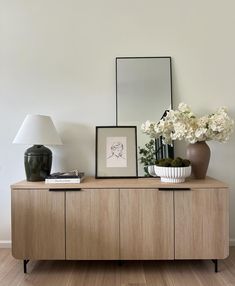 a vase with flowers on top of a wooden cabinet next to a mirror and lamp