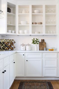 a kitchen with white cabinets and wooden flooring is pictured in this image, there are dishes on the shelves