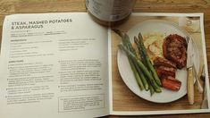 a plate with meat, mashed potatoes and asparagus next to a cup of coffee