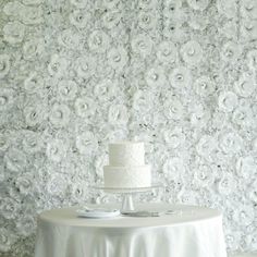 a wedding cake sitting on top of a table next to a white wall covered in flowers