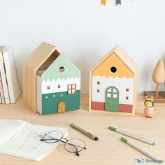 three wooden houses sitting on top of a table next to some books and pencils