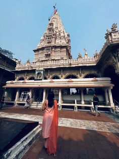 a woman in an orange sari standing outside of a white and gold temple with people walking around