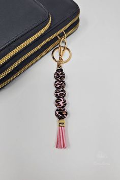 a pink tasseled keychain hanging from a gold chain with a black purse in the background