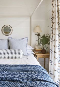 a bed with blue and white comforter in a bedroom next to a lamp on a table