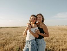 two women hugging each other in the middle of an open field with tall brown grass