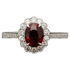 a red and white diamond ring with an oval shaped center surrounded by small round diamonds