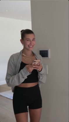 a woman standing in front of a wall holding a cell phone and looking at the camera