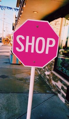 a pink stop sign sitting on the side of a road next to a store front