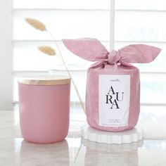 a pink jar with a flower in it next to a cup on a white table