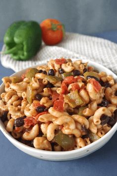 a white bowl filled with pasta and vegetables next to a green pepper on the side