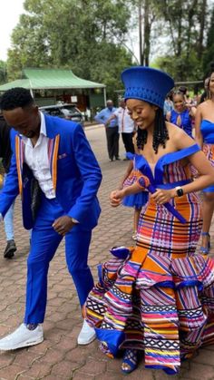 two people in blue and orange dresses dancing on the street with other people standing around