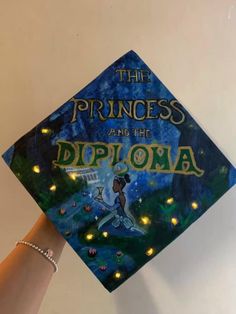 a hand holding up a blue cap with the words princess and the frog on it